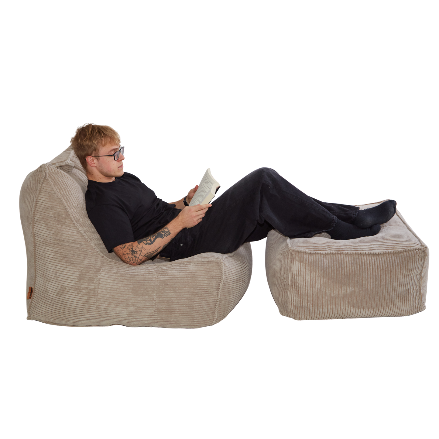 Mężczyzna czytający książkę, siedząc na zestawie eleganckich puf sztruksowych w kolorze beżowym. Zestaw zawiera fotel i pufę wypchane granulatem.