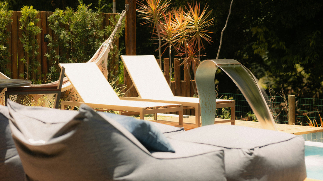 Strefa relaksu przy basenie z dwoma leżakami, leżankami leno i roślinami, w tle wylewka wodna do basenu.