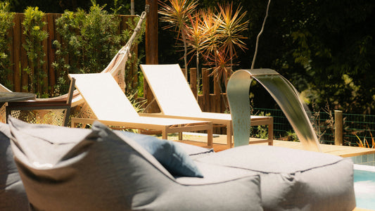 Strefa relaksu przy basenie z dwoma leżakami, leżankami leno i roślinami, w tle wylewka wodna do basenu.