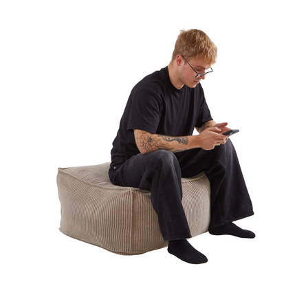 Mężczyzna siedzący na wielkiej, wielofunkcyjnej pufie z tkaniny sztruksowej w kolorze beżowym. 