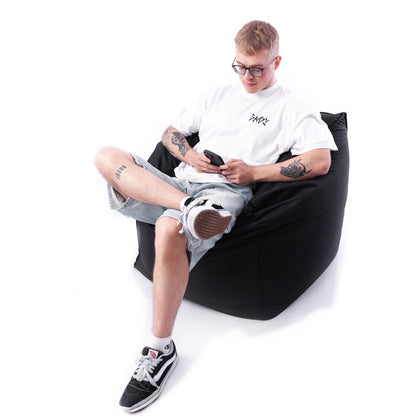 Mężczyzna zrelaksowany na czarnej pufie kostce, idealnej do wnętrz i przestrzeni zewnętrznych – styl i komfort w jednym.