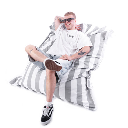 Mężczyzna w okularach przeciwsłonecznych siedzący w pozycji półleżącej na dużej, biało‑szarej poduszce Stripe – pufa outdoor EcoYoung.