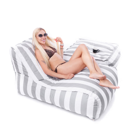 Kobieta w okularach przeciwsłonecznych relaksująca się na biało-szarej leżance Stripe z pufą, idealnej do ogrodu lub nad basen