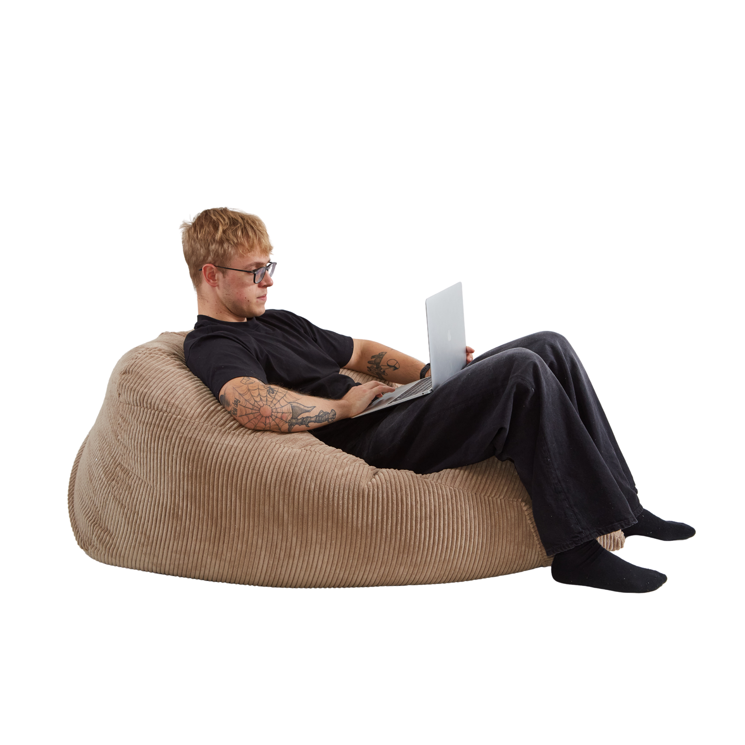 Mężczyzna wygodnie siedzący z laptopem na wielkiej pufie sako z eleganckiej tkaniny sztruksowej w kolorze toffi. 