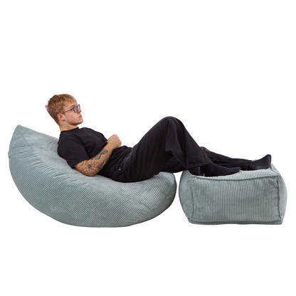 Mężczyzna odpoczywający na zestawie sztruksowych puf. Zestaw zawiera duży fotel-poduchę i pufę w kolorze błękitnym.