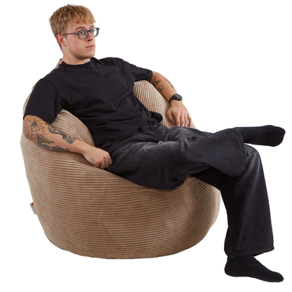 Mężczyzna siedzący na eleganckiej pufie typu worek sako wykonanej z tkaniny sztruksowej w kolorze toffi. 