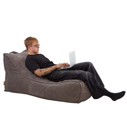 Mężczyzna pracujący na laptopie, leżąc na stylowej leżance Canvas wykonanej z miękkiej tkaniny sztruksowej