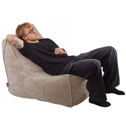 Mężczyzna odpoczywający na wygodnym fotelu LENO z tkaniny sztruksowej w kolorze beżowym.