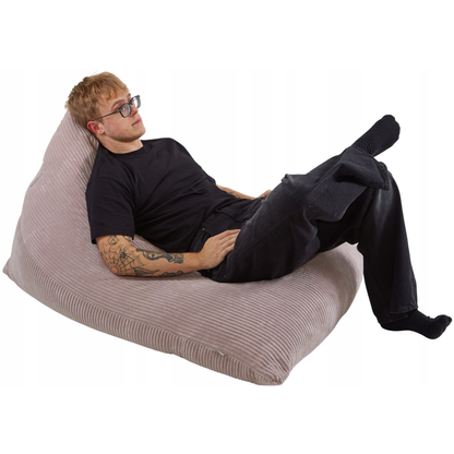 Mężczyzna siedzący na pufie-poduszce Joy wykonanej z tkaniny sztruksowej w kolorze beżowym.