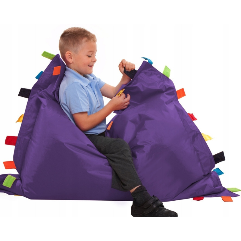 Dziecko bawiące się na fioletowej pufie sensorycznej z doczepionymi pasami z różnych materiałów.