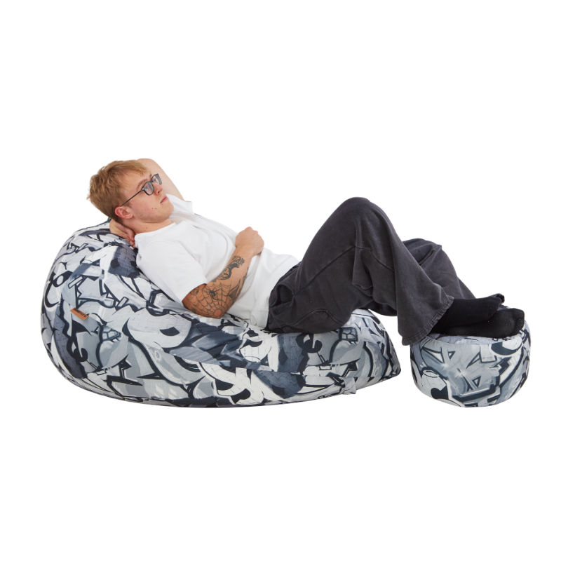 Mężczyzna wygodnie leżący na zestawie puf wypchanych granulatem we wzór z szarym graffiti. 