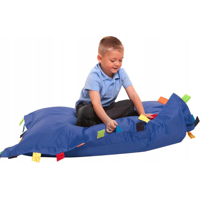 Chłopiec siedzący na niebieskiej pufie sensoryczne, wypchanej granulatem z doczepionym paskami z różnych tkanin. 