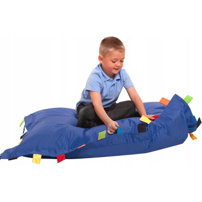 Chłopiec siedzący na niebieskiej pufie sensoryczne, wypchanej granulatem z doczepionym paskami z różnych tkanin. 